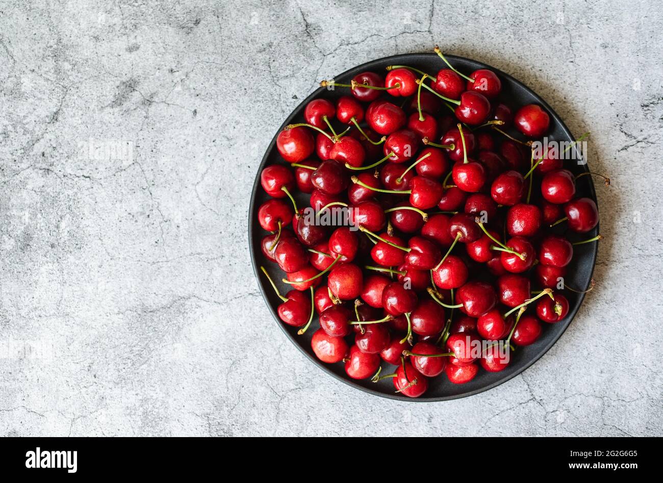 Große Schüssel mit leuchtend roten Kirschen auf einer grauen Zementtheke von oben. Stockfoto