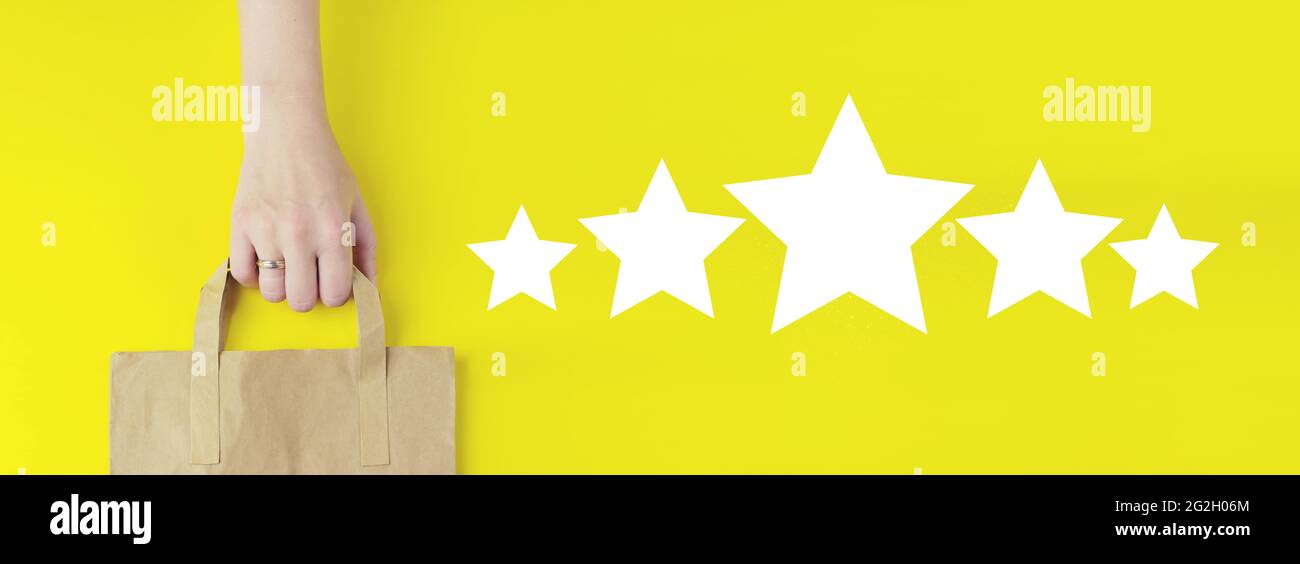 Customer Service Bewertung und Zufriedenheitsumfrage Konzepte.Recycling-braunen Papier Einkaufstasche in der Hand mit Hologramm fünf Sterne 5 Rating-Symbol auf yello Stockfoto