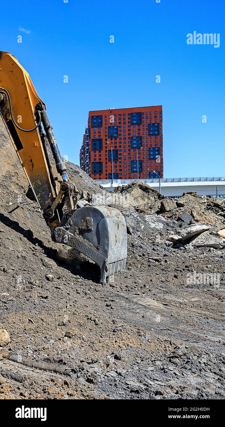 Eimer eines Erdbewegers, der einen Sandhaufen auf dem Hintergrund neuer Häuser gräbt, die auf der Abbruchbaustelle im Bau sind Stockfoto
