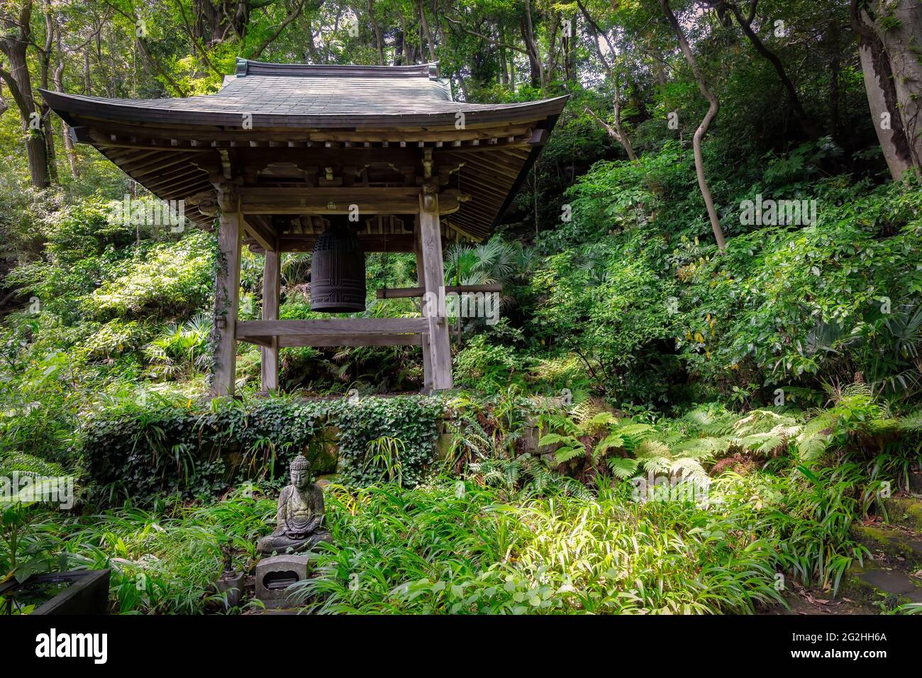 Ein Glockenturm und eine Buddha-Statue sitzen in einem Wald in der Nähe eines Tempels in Kamakura, Japan. Stockfoto