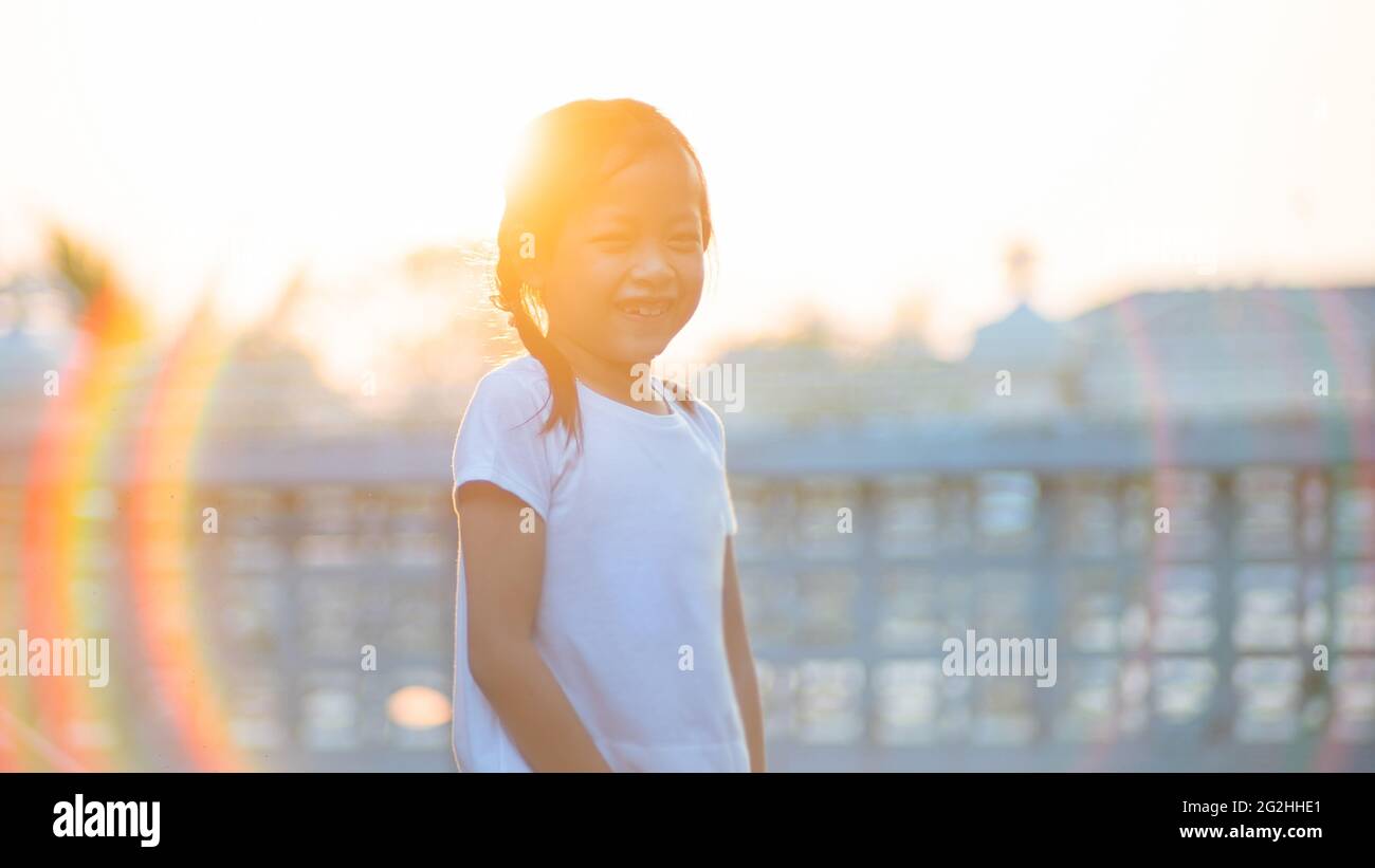 Nette asiatische Kind Mädchen lächeln mit langen Haaren im Sommer im Freien. Haarpracht in den Strahlen des Sonnenuntergangs Stockfoto