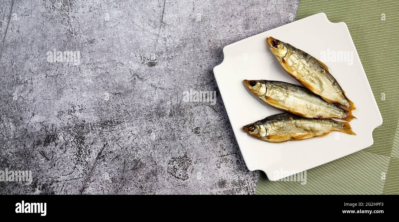 Geräucherter, geschälter Fisch (Coregonus peled) auf einem quadratischen Teller auf dunklem Grund. Draufsicht, flach liegend Stockfoto
