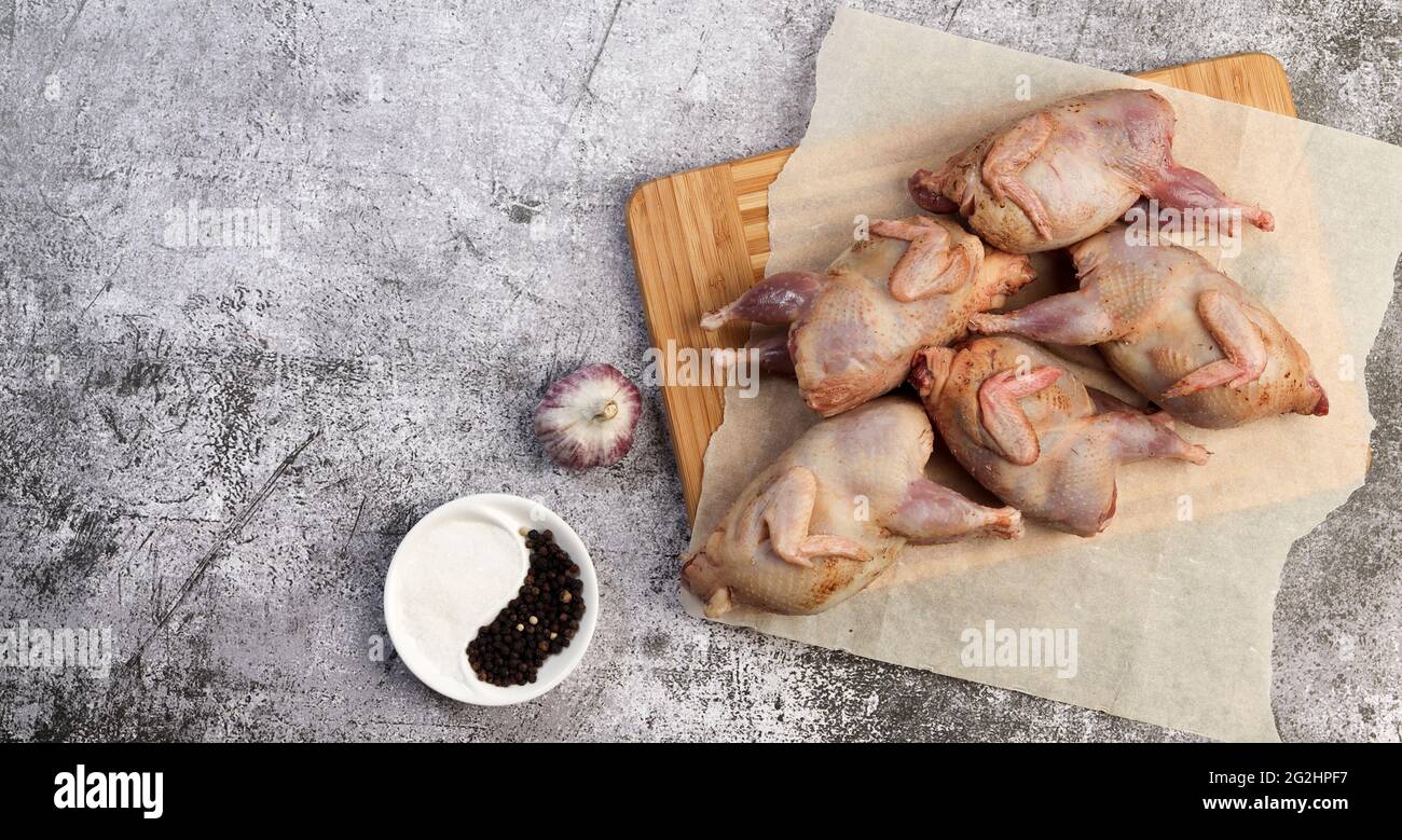 Rohe Wachteln auf einem rechteckigen Holzbrett auf dunklem Hintergrund. Draufsicht, flach liegend Stockfoto