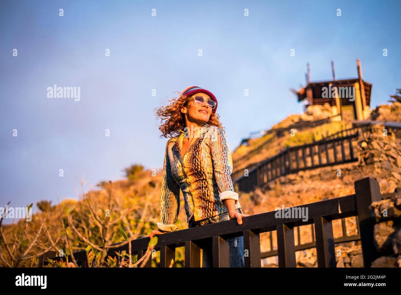 Schöne Frau steht und ejoying den Sonnenuntergang Sonne Licht auf dem Gesicht - Porträt von jungen hübschen weiblichen Menschen im Freien entspannen Freizeitbeschäftigung - Tourist-Look und trendige Kleidung modernen Stil Stockfoto