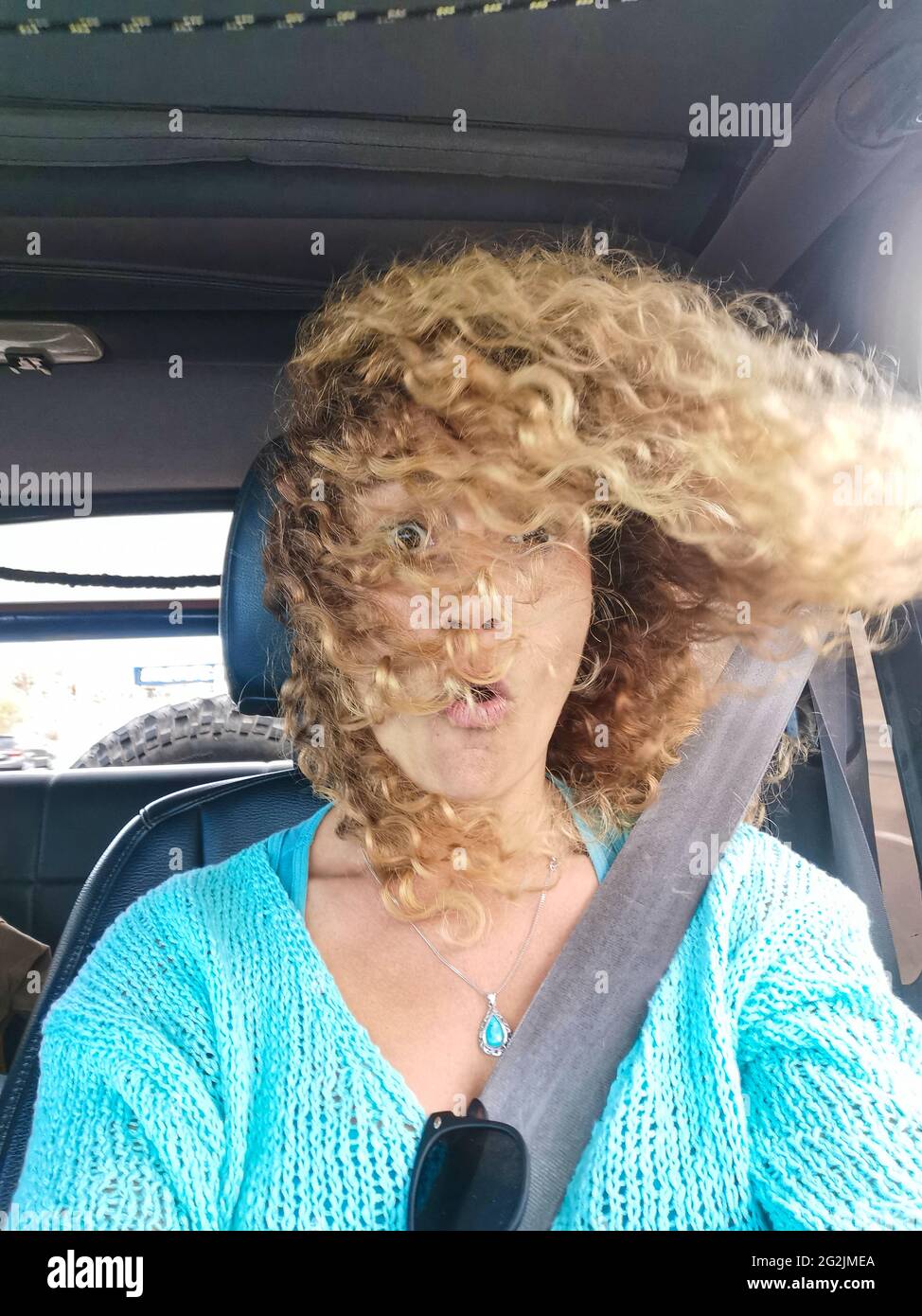 Überrascht Gesichtsausdruck Erwachsene schöne Frau im Auto mit Sicherheitsbelot und Wind bewegen die lockigen Haare - Menschen und Transport Fahrzeug Reise - weibliche Pkw-Passagier im Inneren Stockfoto