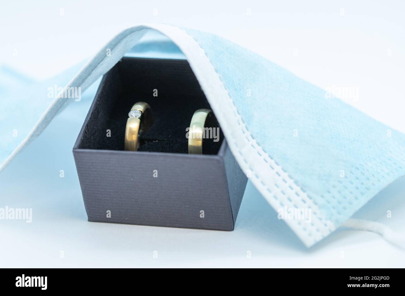 11. Juni 2021, Niedersachsen, Osnabrück: ILLUSTRATION Hochzeitsringe liegen in einer Schachtel unter einer Mund- und Nasenschutzmaske. Seit Anfang Juni sind wieder Feiern mit mehr Gästen erlaubt. Der Inzidenzwert bestimmt, wie viele Personen teilnehmen dürfen. Nach monatelangen Hoffnungen und Ängsten scheinen die Entspannung Niedersachsens das Heil für Brautpaare zu sein. Aber das bleibt auch weiterhin der Fall. (To dpa: 'Entspannung in Niedersachsen: Aber der Hochzeits-Boom bleibt aus') Foto: Friso Gentsch/dpa Stockfoto