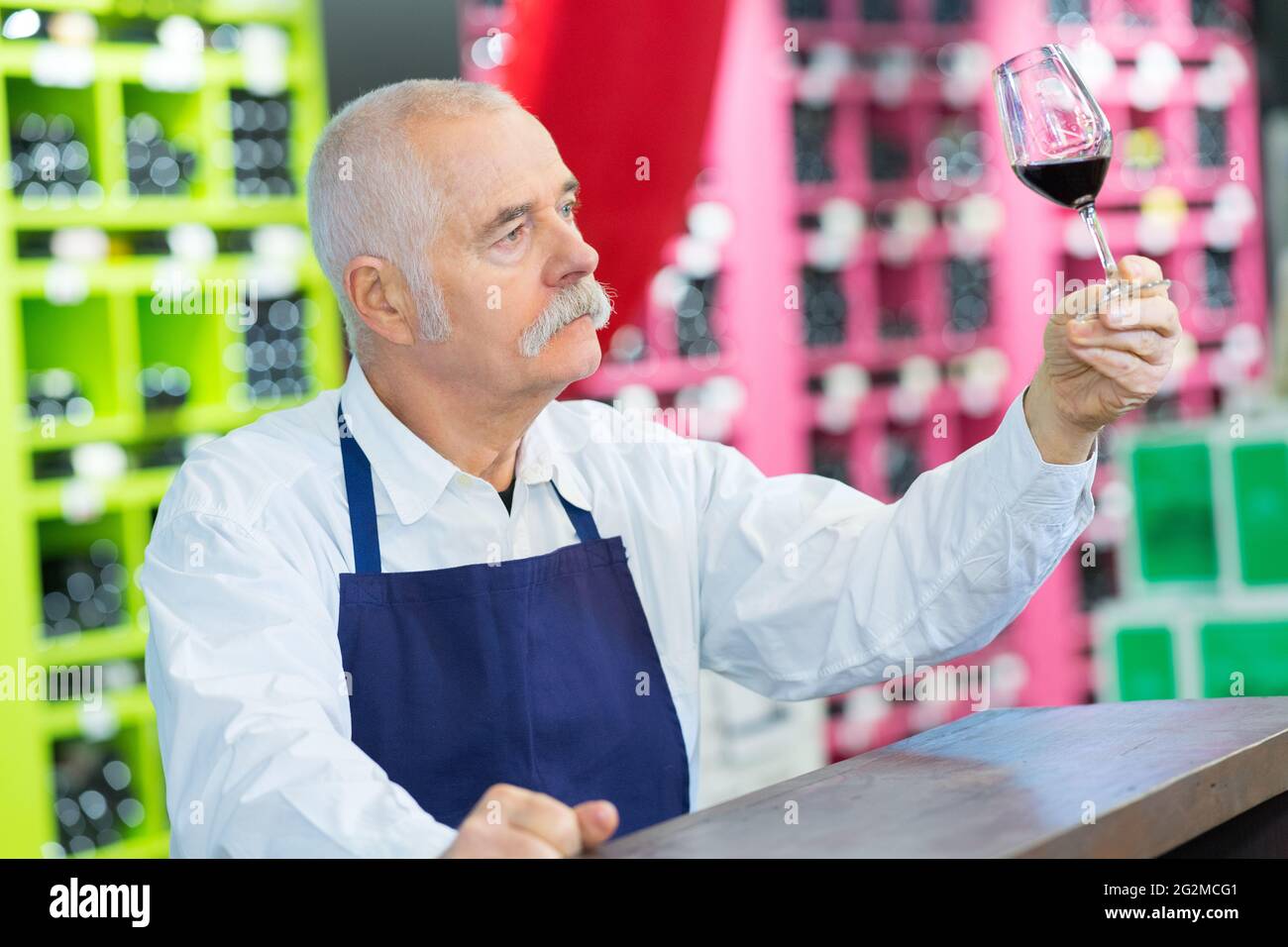 Älterer Mann, der ein Glas Rotwein inspiziert Stockfoto