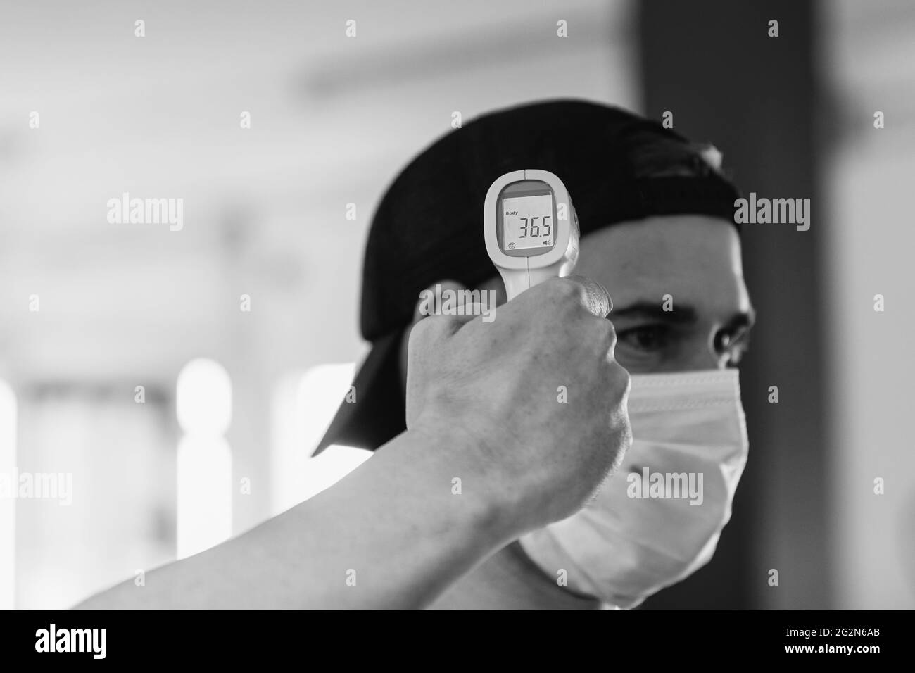 Mann mit Maske nimmt seine Temperatur. Infrarot-Thermometer. Gesundes Fitnessstudio. Pandemie, Coronavirus. Konzept von Gesundheit und Sicherheit Stockfoto