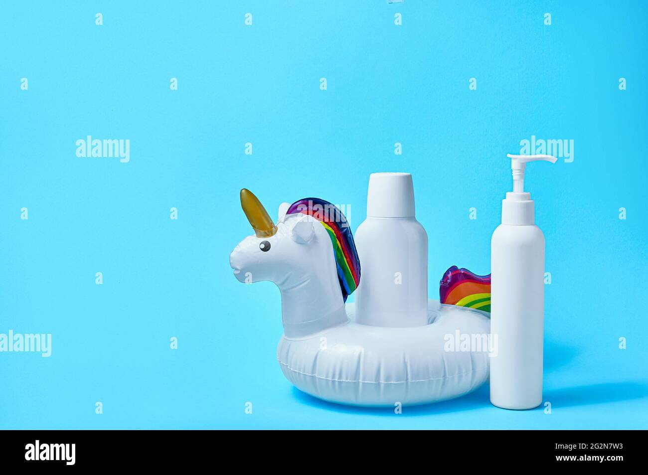 Sonnenschutzflasche mit aufblasbarem weißen Einhorn-Poolspielzeug auf blauem Hintergrund. Kreatives Minimalkonzept. Stockfoto