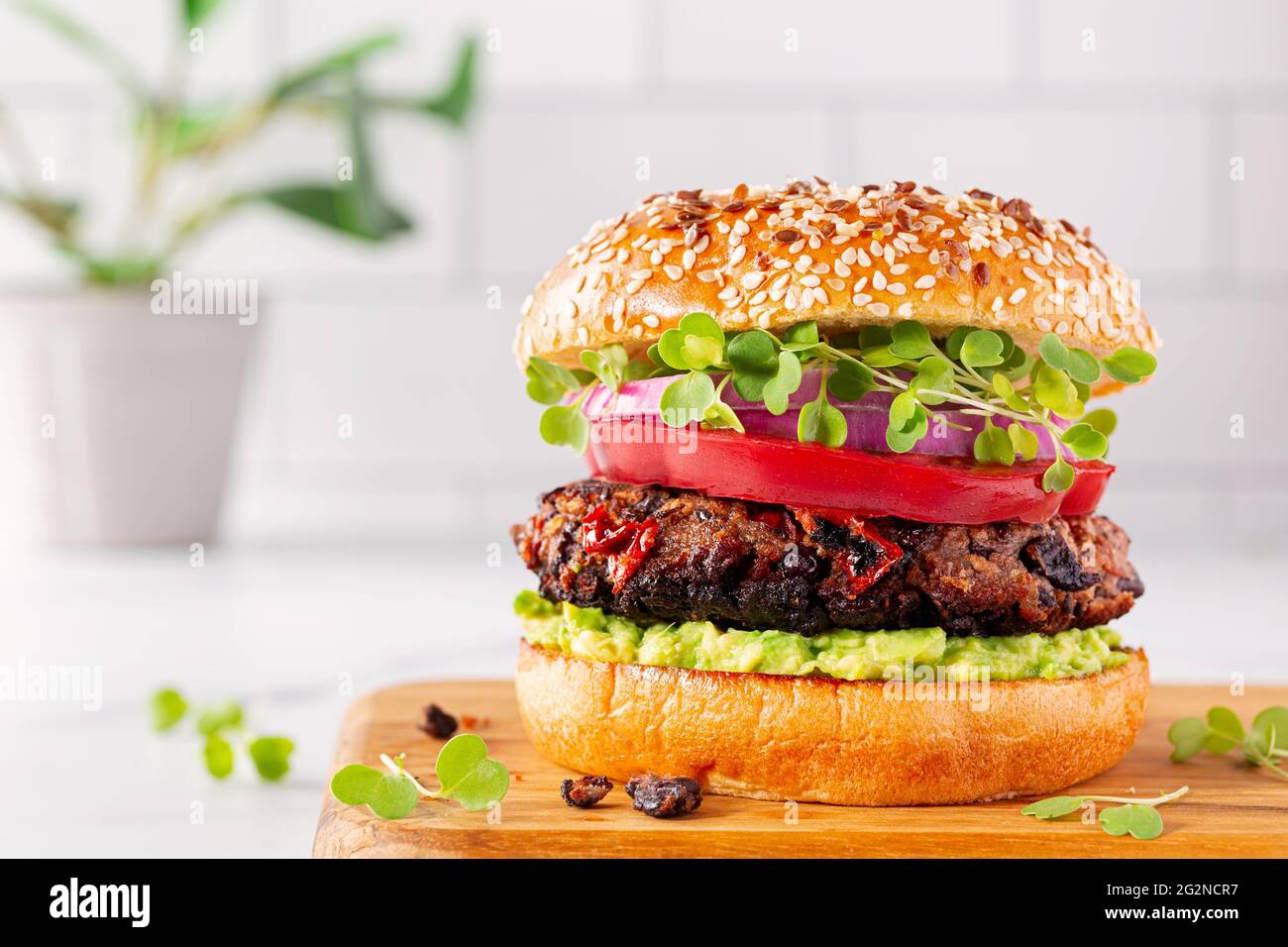 Pflanzenbasierter Avocado-Burger mit schwarzen Bohnen auf Sesambrötchen mit Tomaten, Mikrogemüse und roten Zwiebeln Stockfoto