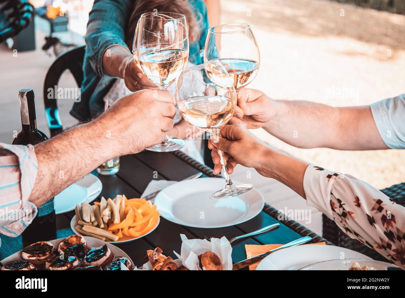 Schneiden Sie Nahaufnahme der Hände von Freunden auf der Terrasse bei einem Glas Weißwein. Gemeinsames Urlaubskonzept Stockfoto