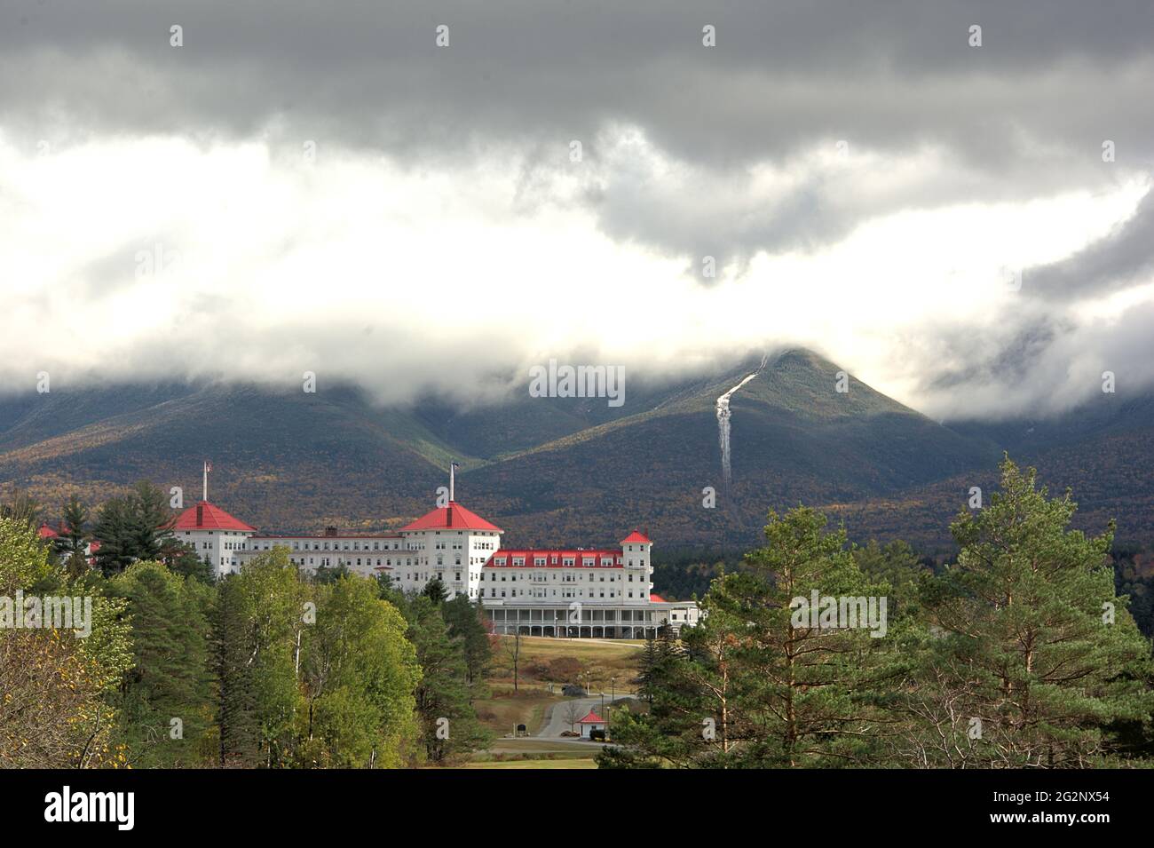 Rotes Dach eines der verbleibenden Grand Hotels in den White Mountains von New Hampshire mit bedrohlichen Sturmwolken, die Mount Washington umhüllen. Stockfoto