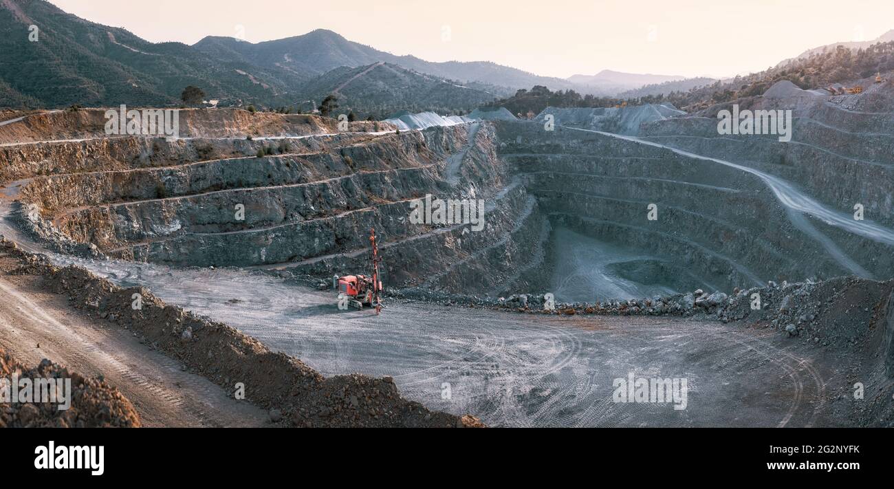 Kiesgrube mit Terrassen, Steinhaufen und roter Brechmaschine. Panorama mit Berghintergrund in der Dämmerung Stockfoto