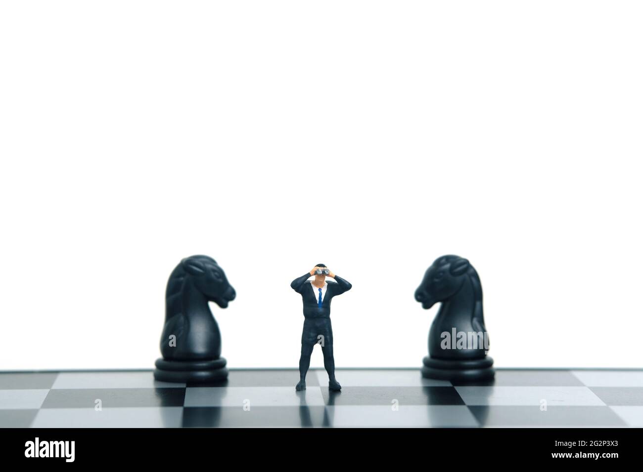 Geschäftsmann mit Fernglas, der zwischen dem Pferderitter und dem Schachpfand steht. Miniatur winzigen Menschen Spielzeug Fotografie. Isoliert auf weißem Hintergrund. Stockfoto