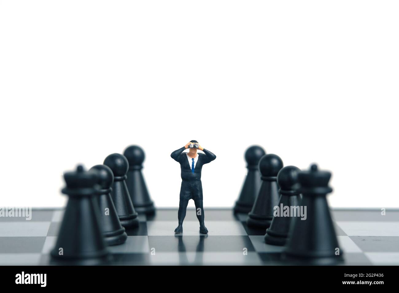 Geschäftsmann mit Fernglas, der zwischen dem Schachpfand steht. Miniatur winzigen Menschen Spielzeug Fotografie. Isoliert auf weißem Hintergrund. Stockfoto
