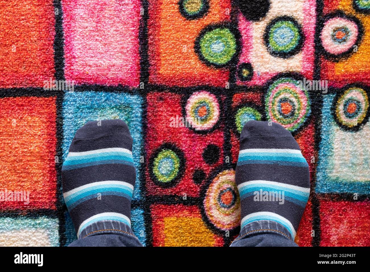 Füße eines Mannes in Socken am Rand eines bunt gemusterten Teppichs mit Platz für Kopien. Thema: Am Rande, ein neues Abenteuer, geerdet in der Realität Stockfoto