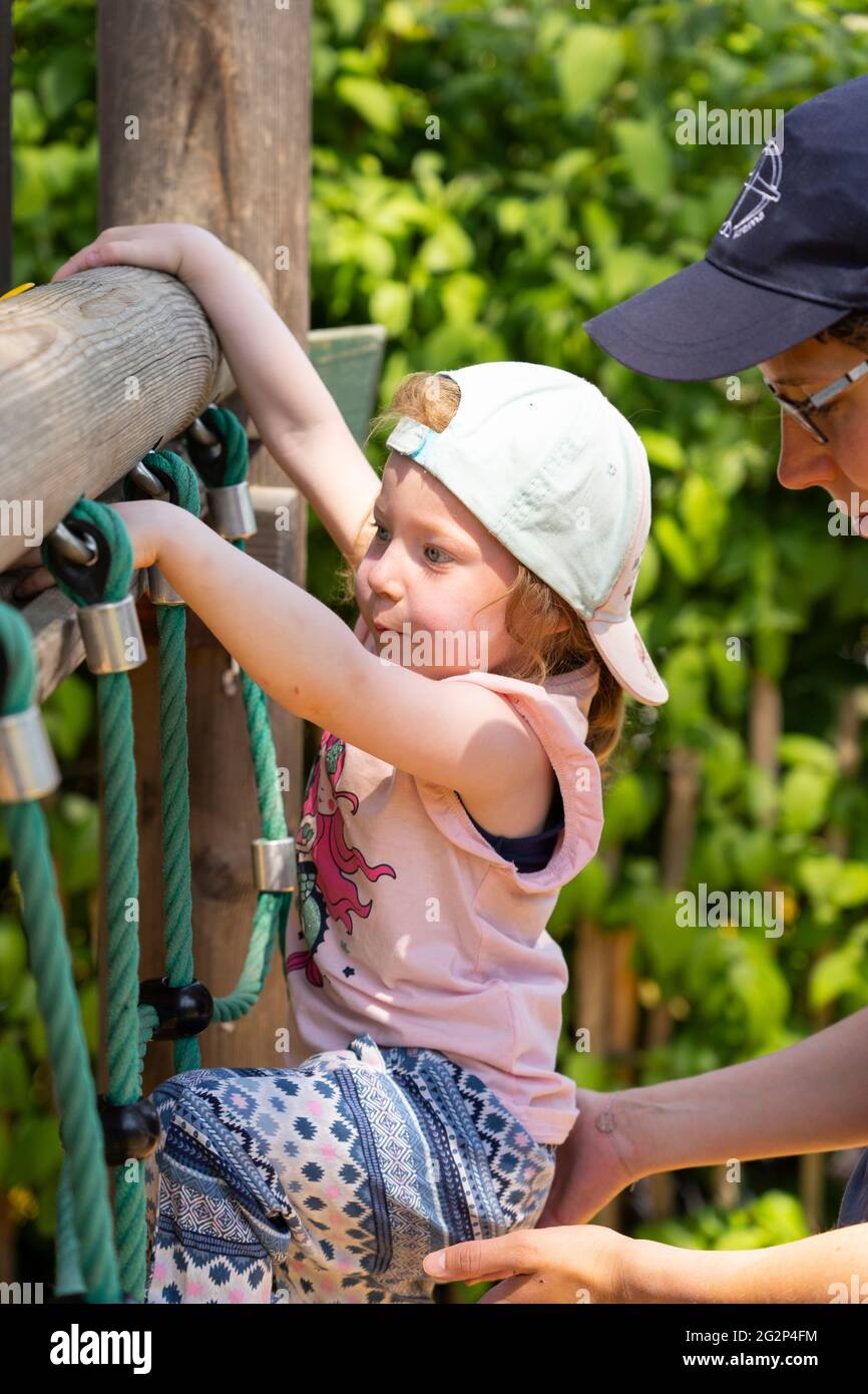 Eine Mutter hilft ihrem 3-jährigen Kind, Seile auf einem Klettergerüst zu klettern. Thema: Mutter-Kind-Beziehung, elterliche Führung, Lehren, Lernen Stockfoto