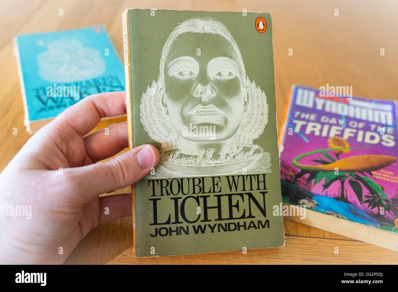 Eine Männerhand, die einen Taschenbuch von Ärger mit Lichen hält, ein Roman des englischen Science-Fiction-Autors John Wyndham aus dem Jahr 1960 Stockfoto