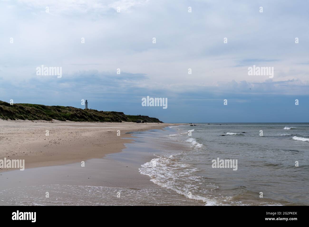 Ein wunderschöner weißer Sandstrand mit einem Leuchtturm im Hintergrund hoch oben auf grasbewachsenen Sanddünen Stockfoto