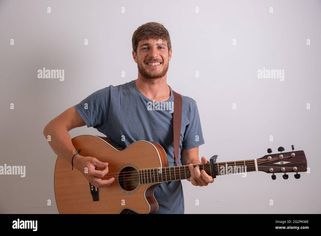 Porträt eines jungen Musikers, der Gitarre spielt und lächelt. Studiofoto eines Künstlers isoliert auf weißem Hintergrund. Junger lächelnder Mann. Stockfoto
