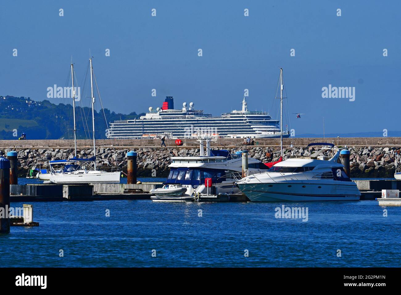 Brixham, Großbritannien. 12th. Juni 2021. UK.Brixham Devon. Während der Covid-19-Einschränkungsbedingungen schwebt Ein Küstenwache-Hubschrauber vor dem MS Queen Victoria Cunard Line-Kreuzschiff, während er auf See in der Brixham Bay festmacht. ? Bildquelle: Robert Timoney/Alamy Live News Stockfoto
