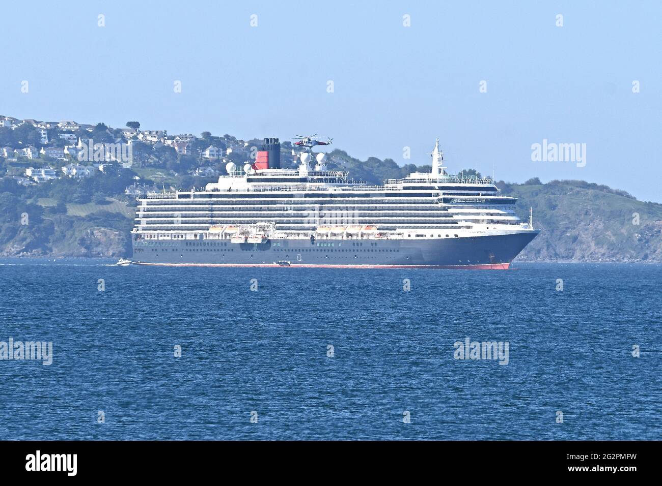 Brixham, Großbritannien. 12th. Juni 2021. UK.Brixham Devon. Während der Covid-19-Einschränkungsbedingungen schwebt Ein Küstenwache-Hubschrauber vor dem MS Queen Victoria Cunard Line-Kreuzschiff, während er auf See in der Brixham Bay festmacht. ? Bildquelle: Robert Timoney/Alamy Live News Stockfoto