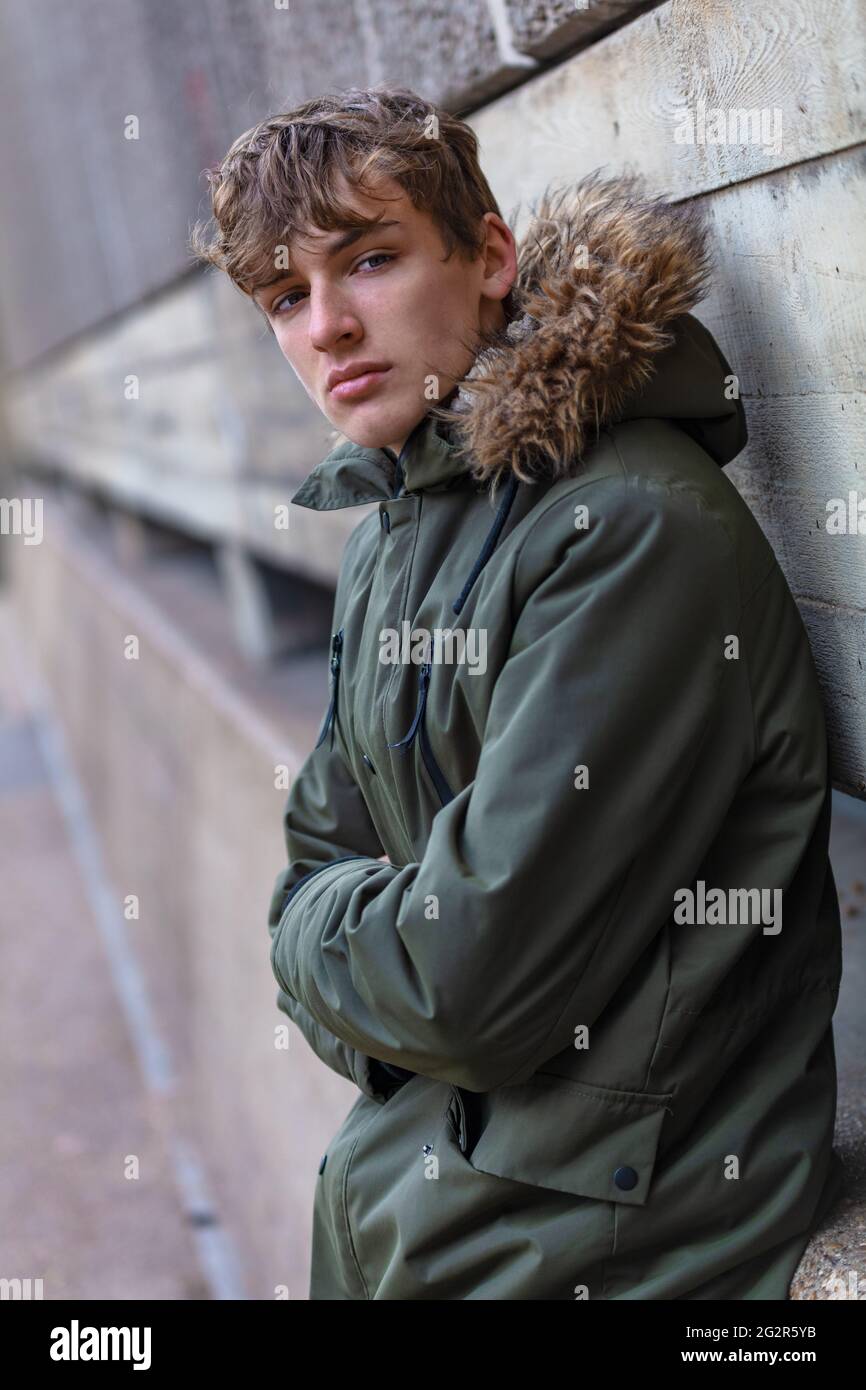 Männlicher junger Erwachsener Teenager, der eine Parka-Jacke trägt, draußen in einer modernen städtischen Umgebung Stockfoto