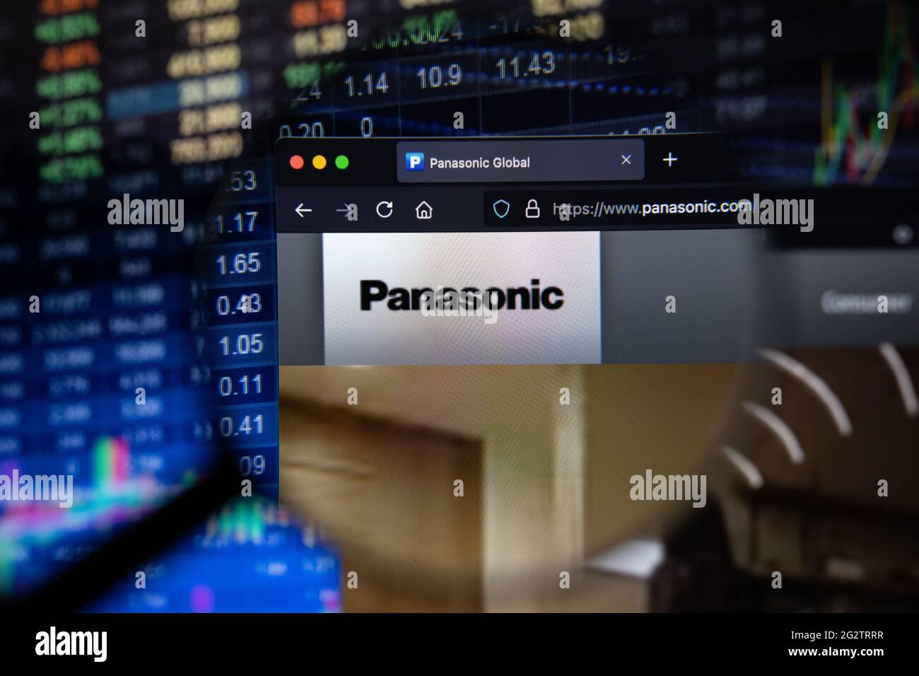 Panasonic Firmenlogo auf einer Website mit verschwommenen Börsenentwicklungen im Hintergrund, die auf einem Computerbildschirm durch eine Lupe gesehen werden Stockfoto