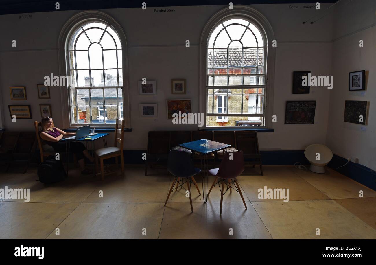 Inneneinrichtung des Gallerie-Cafés mit Bogenfenstern, Gemälden an der Wand und einer Frau, die am Laptop arbeitet. Stockfoto