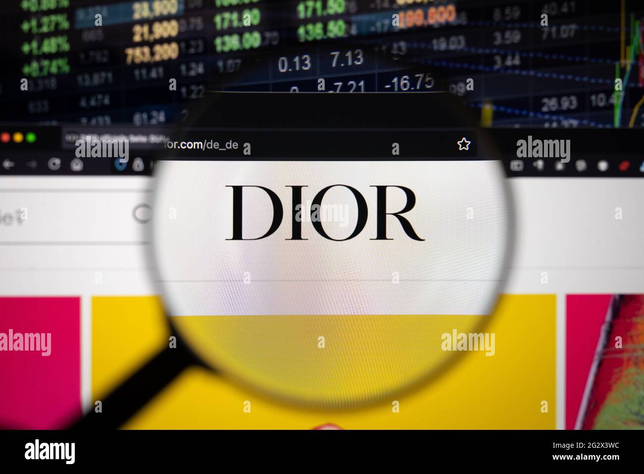 Dior-Firmenlogo auf einer Website mit verschwommenen Börsenentwicklungen im Hintergrund, die auf einem Computerbildschirm durch eine Lupe gesehen werden Stockfoto