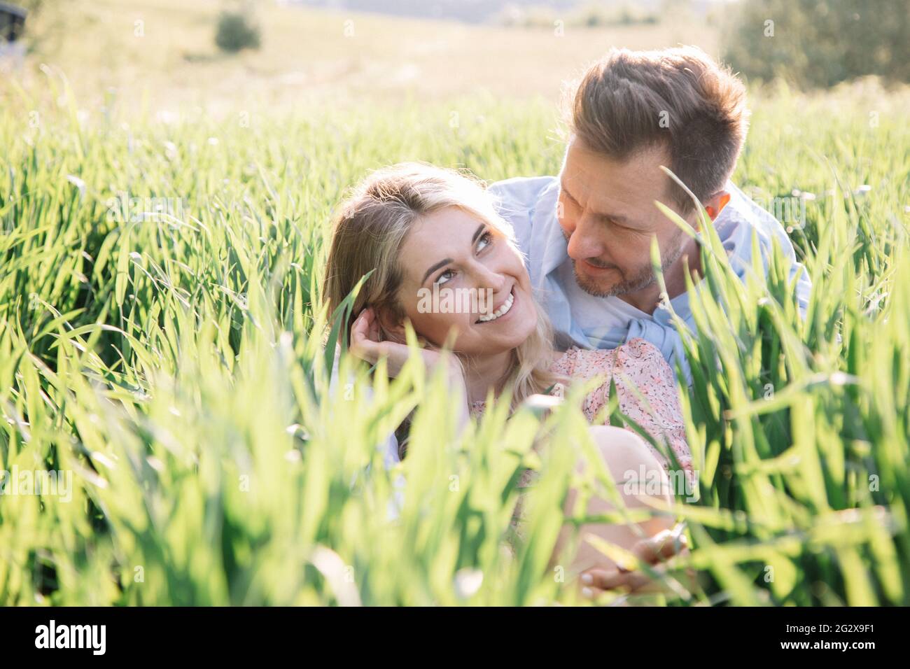 Schöne junge Frau flirtet mit ihrem Mann, während sie im Gras sitzt, Lifestyle-Porträt Stockfoto