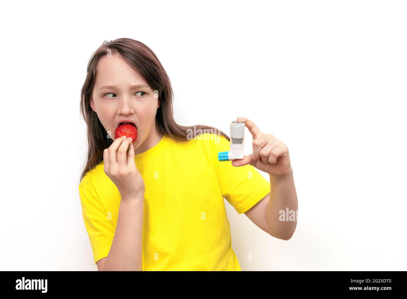 Ein 10-jähriges Mädchen hält Erdbeeren in den Händen und schaut vor Angst auf weißem Hintergrund auf den Asthmainhalator. Konzept für Lebensmittelallergien Stockfoto