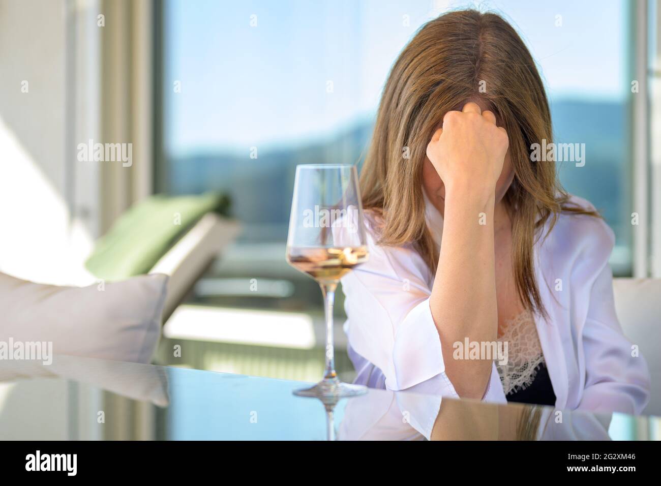 Depressive Frau, die tief mit einem Glas Rotwein vor ihrem Gesicht sitzt und ihre Stirn auf der Hand hält Stockfoto
