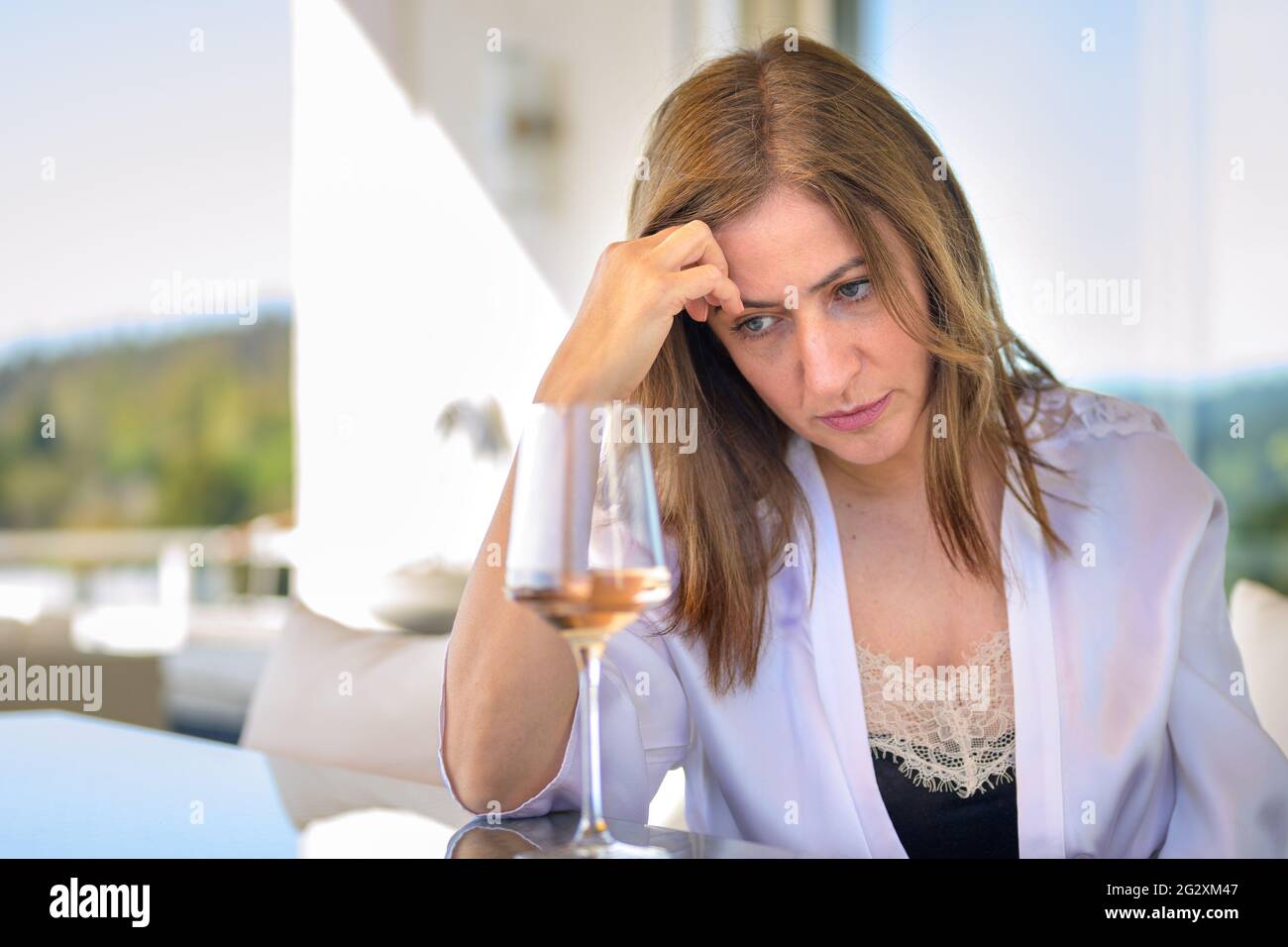 Depressive Frau, die tief mit einem Glas Rotwein vor ihr sitzt und ihre Stirn auf der Hand legt und auf den Tisch starrt Stockfoto