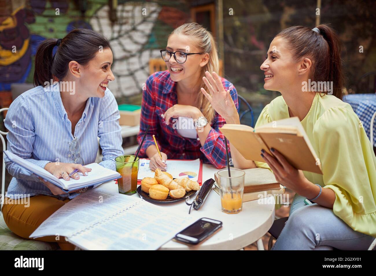 Drei junge Erwachsene kaukasische Frauen studieren zusammen im Café im Freien, lächeln, lachen, reden Stockfoto