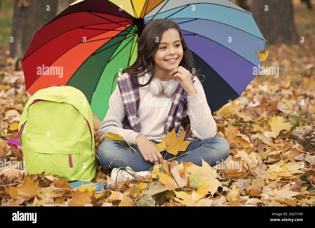 Schnapper Erinnerungen. Genießen Sie warmes saisonales Wetter. Happy Kid  sitzt unter bunten Regenschirm. Mädchen mit Rucksack unter Regenschutz.  Kind entspannen Stockfotografie - Alamy