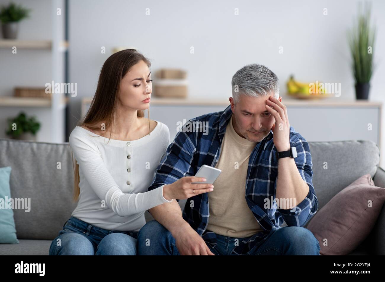 Reife Frau konfrontiert ihren Mann über die Korrespondenz mit seinem Geliebten auf dem Smartphone Stockfoto