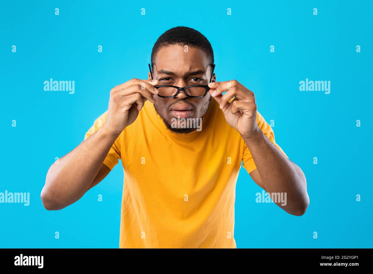 Afroamerikanischer Mann, Der Augen Schielt Und Durch Die Brille Schaut, Blauer Hintergrund Stockfoto