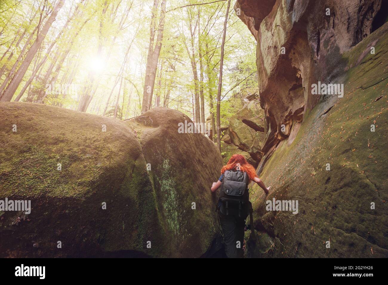 Die rothaarige junge Frau mit Rucksack genießt ihren Weg im grünen Frühlingswald. Konzept des aktiven Lebens. Stockfoto