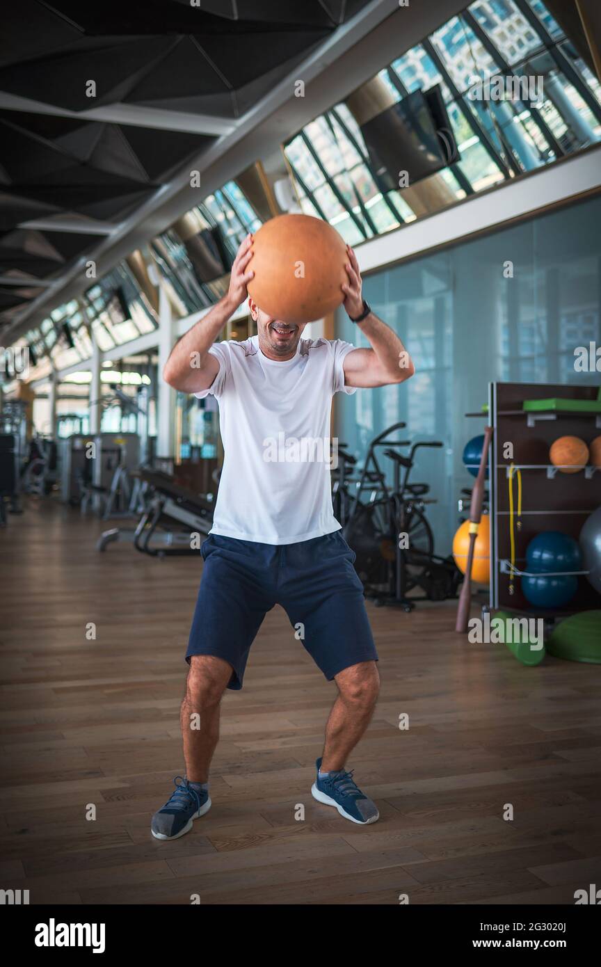 Mann, der im Fitnessstudio trainiert, springt und knallt einen schweren Medizin-Slam-Ball für Kernkraftübungen Stockfoto