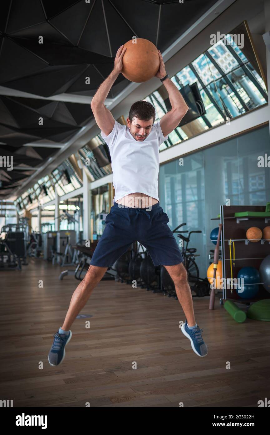 Mann, der im Fitnessstudio trainiert, springt und knallt einen schweren Medizin-Slam-Ball für Kernkraftübungen Stockfoto