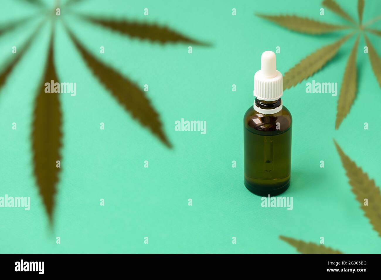 Grüne Marihuanablätter auf grünem Hintergrund mit Cannabisöl in einer Glasflasche, selektiver Fokus. Cannabis für medizinische Zwecke Konzept Stockfoto