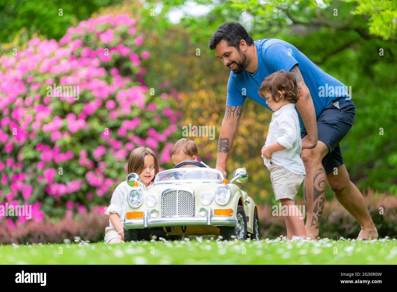 Papa mit drei jungen Söhnen spielt draußen mit einem Spielzeug-Elektroauto Stockfoto