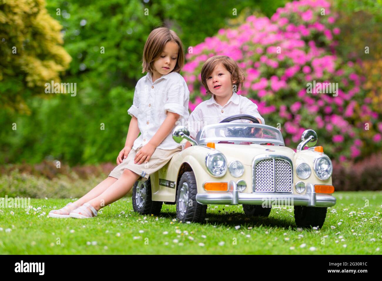 Zwei junge Brüder im Alter von sechs und drei Jahren spielen draußen mit einem Spielzeug-Elektroauto Stockfoto