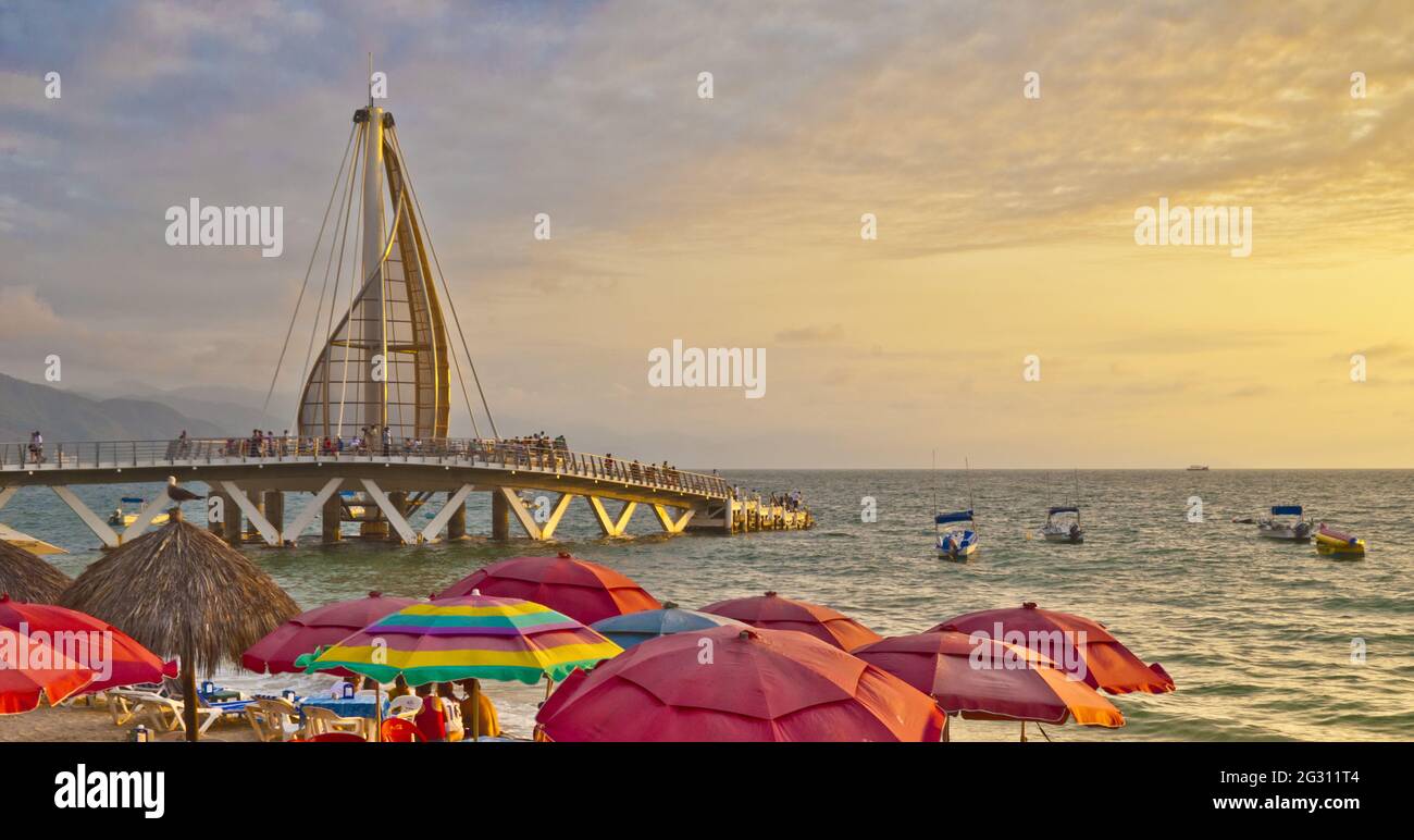 Die Segelskulptur und der Pier wechseln nachts die Farben - 2013 eingeweiht und vom mexikanischen Architekten Jesus Torres Vega entworfen, mit Blick auf die Sonnenschutze am Strand Stockfoto