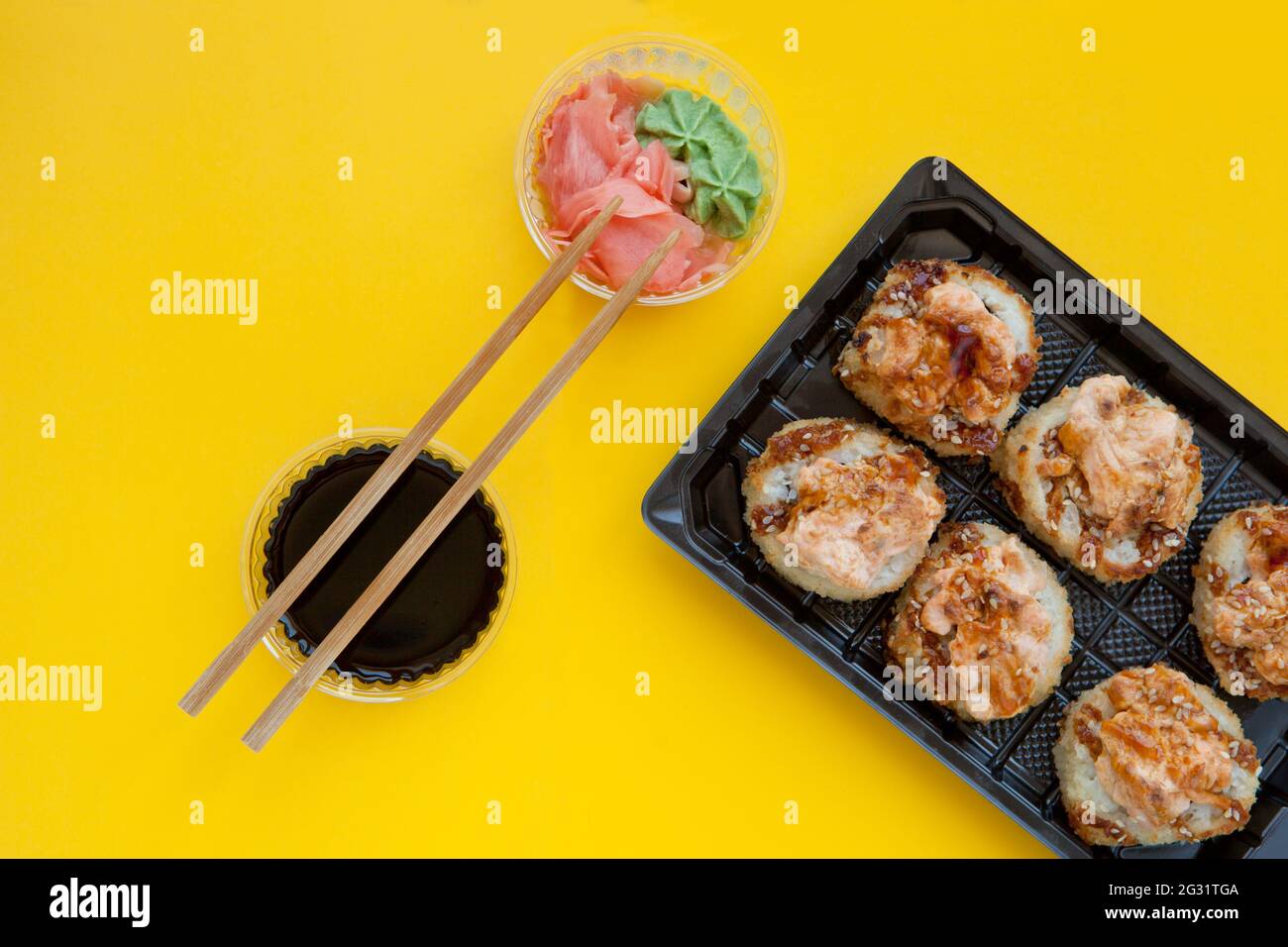Flaches Lay-Set mit Ingwer und Wasabi - gebackenes Sushi-Set mit Lachs in Kunststoffverpackung auf gelbem Hintergrund - Hell leckeres Set von Sushi-Rollen in einem Stockfoto