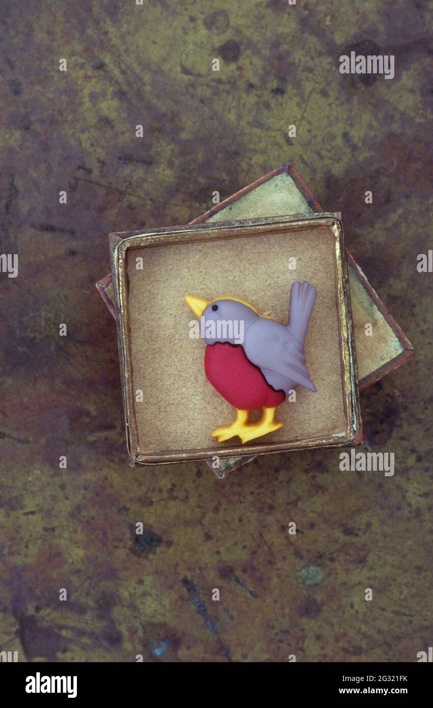 Kleines Modell eines Vogels wie ein Europäischer Rotkehlchen, der in einer Pappschachtel auf angeschlammtem Messing steht Stockfoto