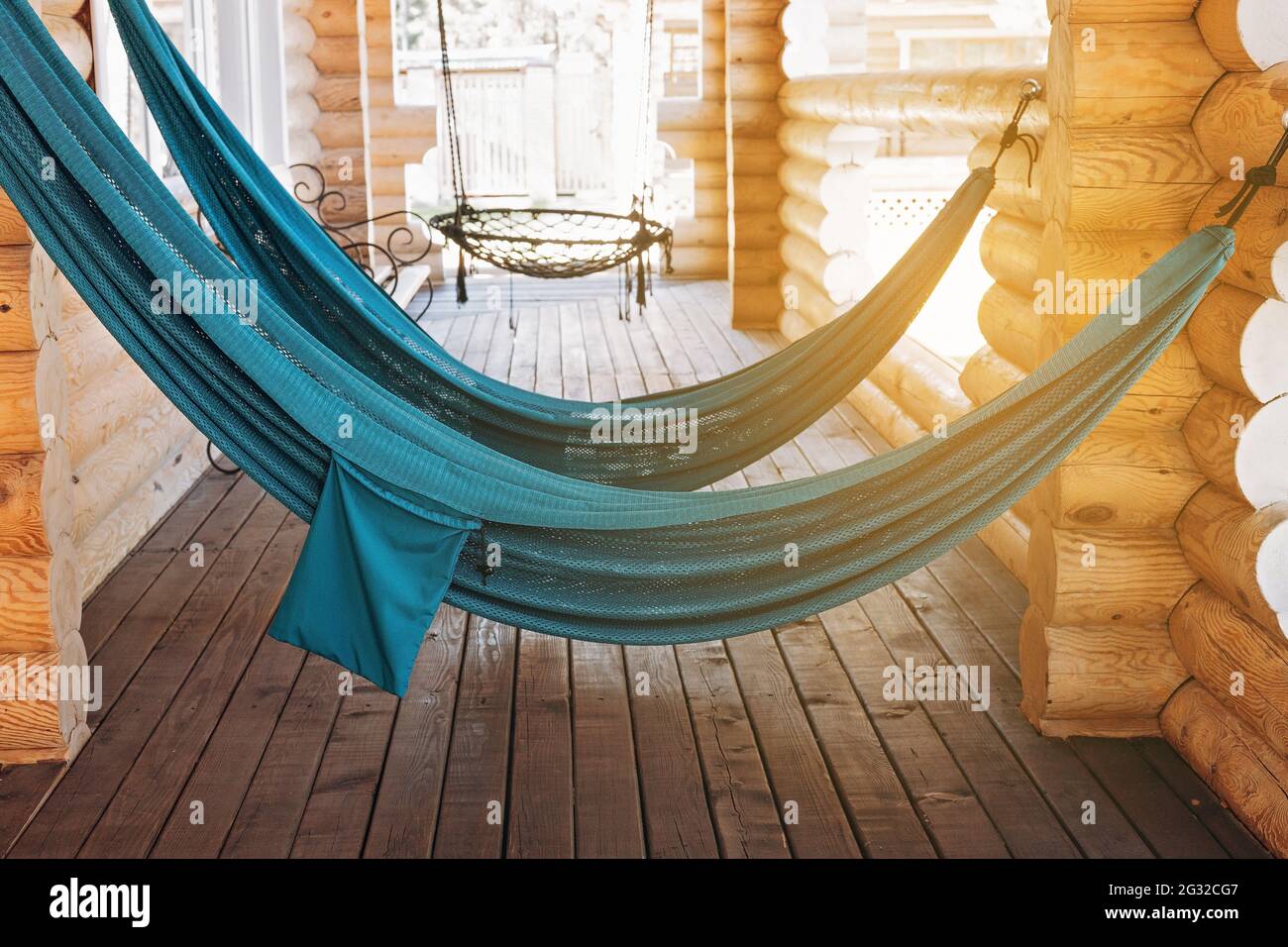 Hängende Hängematten zum Entspannen auf der offenen Terrasse eines Holzhauses. Erholung auf dem Land und Entspannung in der Natur im Sommer. Speicherplatz kopieren. Stockfoto