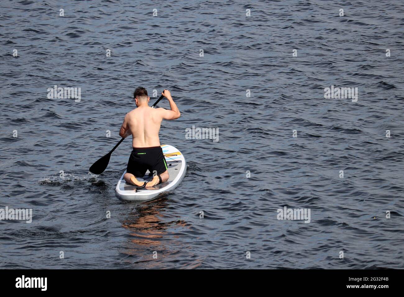 SUP-Surfen, muskulöser Mann mit Paddel, der auf einem Brett im Wasser kniet. Stand-up-Paddleboarding, Sommerurlaub Stockfoto