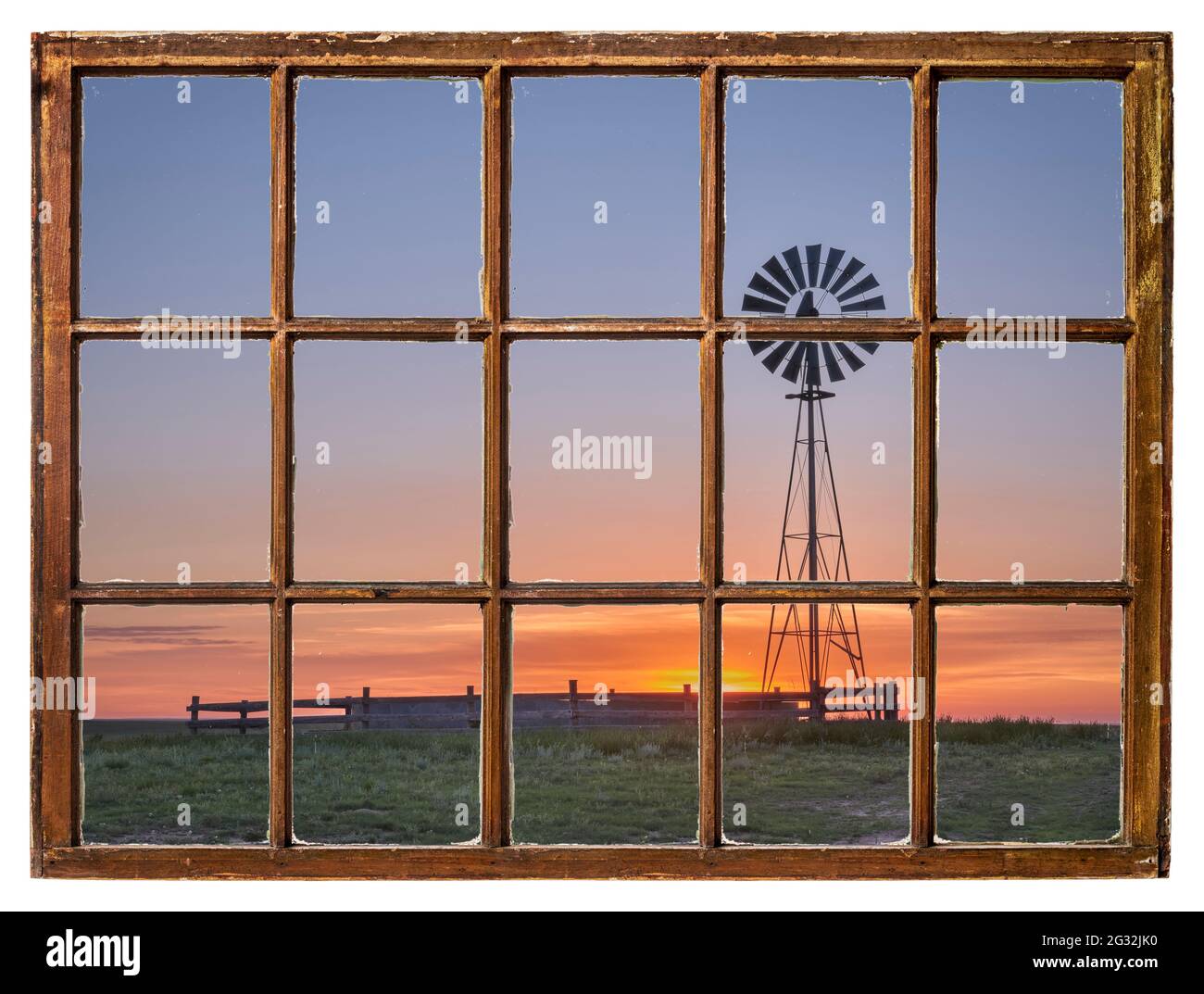 Windmühle mit Wasserpumpe und Tank gegen Sonnenaufgang in einer Prärie, wie vom Vintage-Schiebefenster aus gesehen Stockfoto